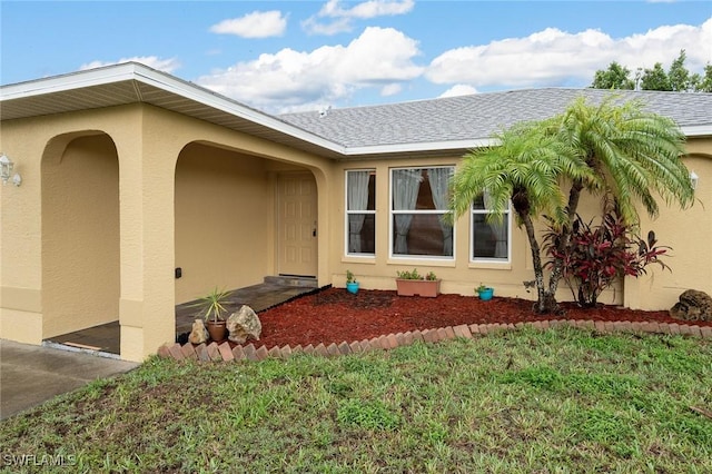 doorway to property featuring a yard, roof with shingles, and stucco siding