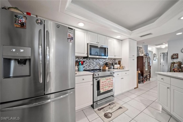 kitchen with decorative backsplash, appliances with stainless steel finishes, a raised ceiling, white cabinetry, and light tile patterned flooring