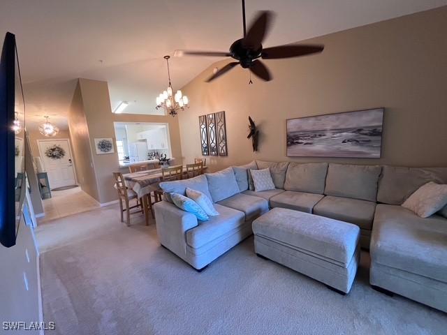 living room featuring ceiling fan with notable chandelier, carpet, and vaulted ceiling