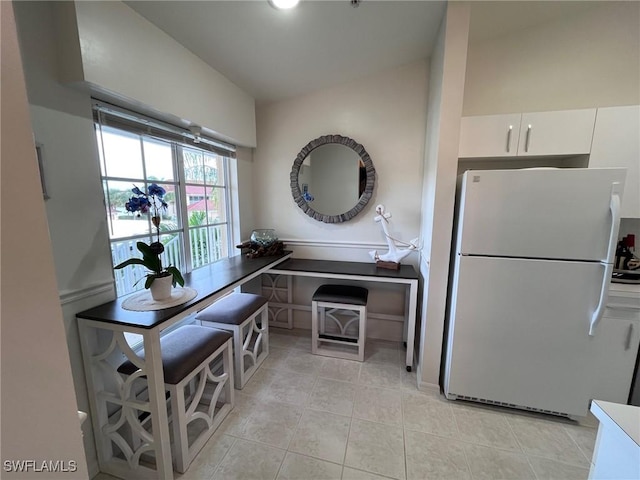 kitchen with white cabinetry, light tile patterned floors, and freestanding refrigerator