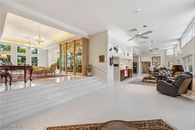 tiled living room with ceiling fan with notable chandelier, a raised ceiling, and crown molding