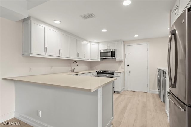 kitchen featuring white cabinetry, sink, kitchen peninsula, light hardwood / wood-style floors, and appliances with stainless steel finishes