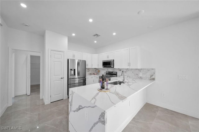 kitchen featuring sink, kitchen peninsula, decorative backsplash, white cabinets, and appliances with stainless steel finishes