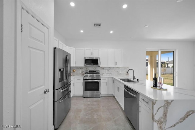 kitchen with kitchen peninsula, appliances with stainless steel finishes, decorative backsplash, sink, and white cabinetry