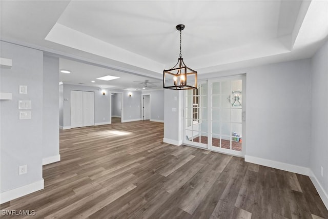 unfurnished dining area with wood-type flooring, ceiling fan with notable chandelier, and a raised ceiling