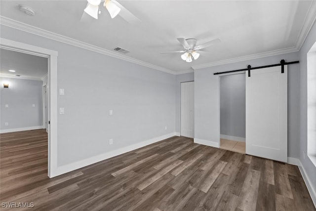 unfurnished bedroom featuring a barn door, dark hardwood / wood-style floors, ceiling fan, and crown molding