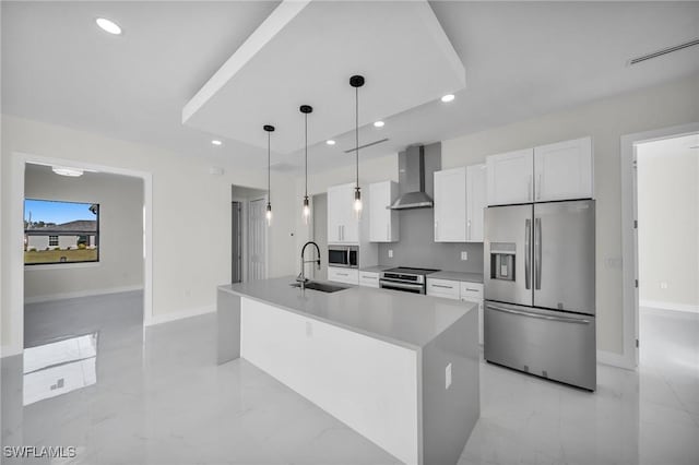 kitchen featuring wall chimney exhaust hood, stainless steel appliances, decorative light fixtures, a center island with sink, and white cabinetry