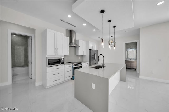 kitchen with wall chimney exhaust hood, stainless steel appliances, pendant lighting, a center island with sink, and white cabinetry