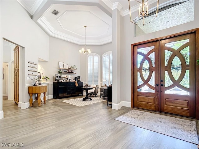 entryway featuring french doors, a notable chandelier, crown molding, a towering ceiling, and light wood-type flooring