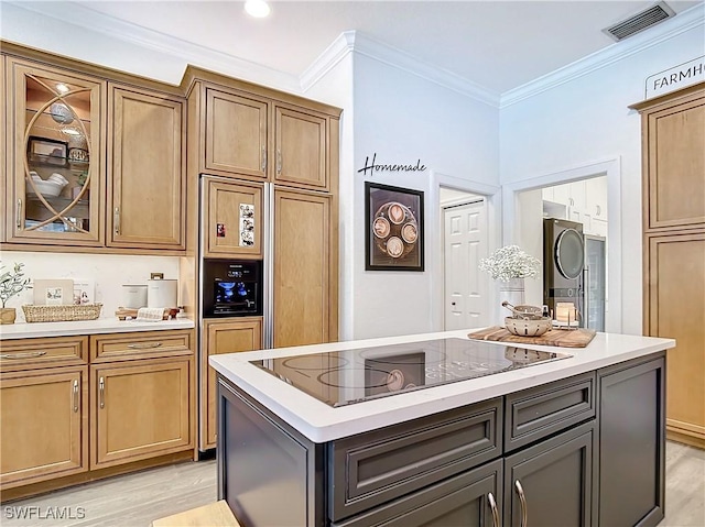 kitchen featuring a center island, black electric stovetop, light wood-type flooring, ornamental molding, and stacked washer / drying machine