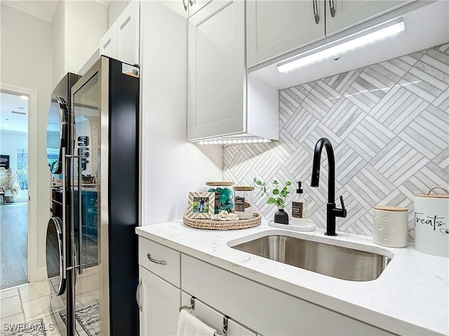 kitchen featuring light stone counters, washer and clothes dryer, sink, white cabinets, and stainless steel refrigerator