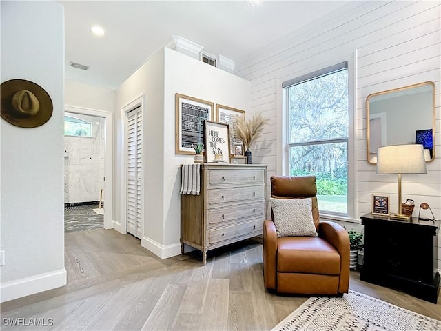 sitting room featuring wood walls, a wealth of natural light, and light hardwood / wood-style flooring