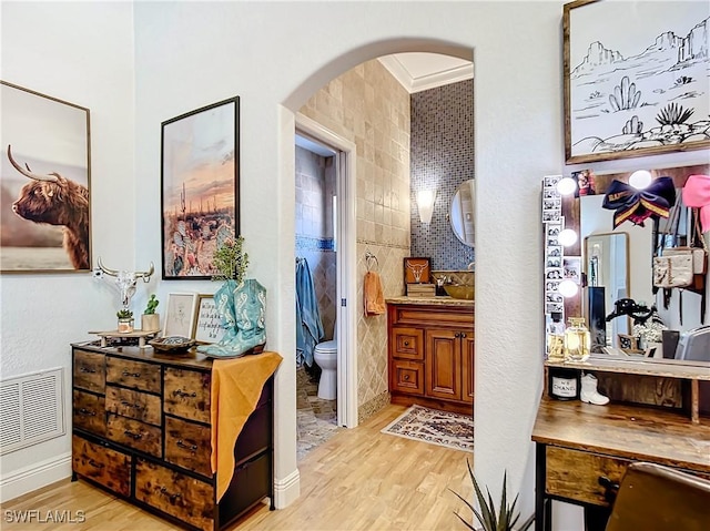 hall featuring light hardwood / wood-style floors, ornamental molding, and tile walls