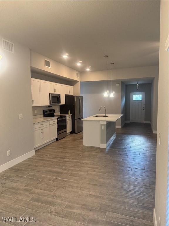 kitchen with pendant lighting, hardwood / wood-style floors, a kitchen island with sink, sink, and appliances with stainless steel finishes