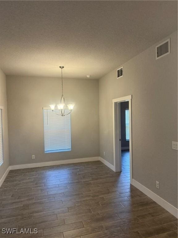 unfurnished room with a textured ceiling, dark wood-type flooring, and an inviting chandelier