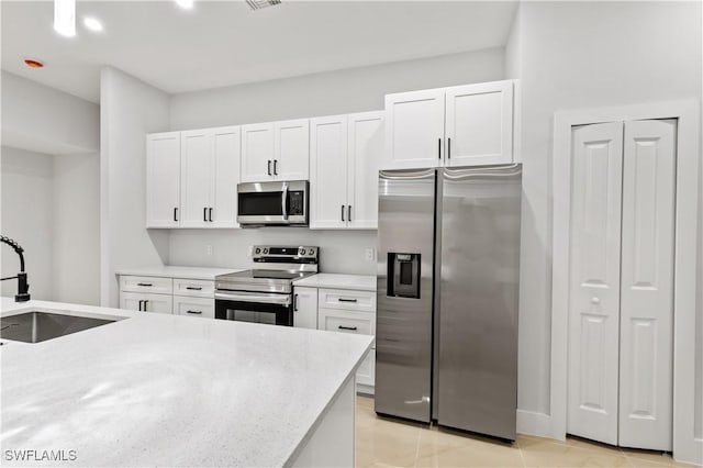 kitchen with light stone countertops, sink, light tile patterned floors, white cabinets, and appliances with stainless steel finishes