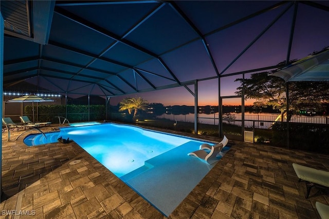 pool at dusk featuring glass enclosure and a patio area