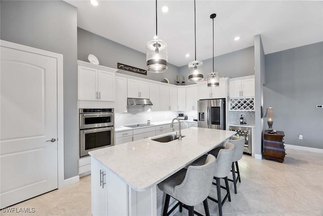 kitchen featuring stainless steel appliances, sink, pendant lighting, white cabinets, and an island with sink