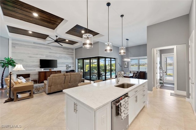 kitchen with white cabinetry, sink, light stone counters, decorative light fixtures, and a center island with sink