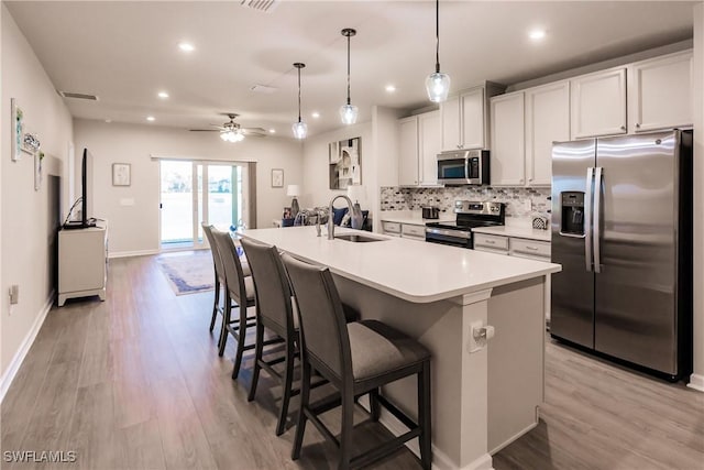 kitchen featuring ceiling fan, sink, hanging light fixtures, stainless steel appliances, and a kitchen island with sink