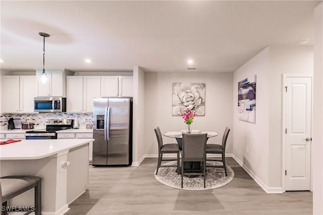 kitchen featuring white cabinetry, stainless steel appliances, a kitchen breakfast bar, light hardwood / wood-style flooring, and decorative light fixtures