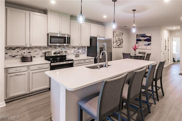 kitchen with hanging light fixtures, sink, appliances with stainless steel finishes, and an island with sink