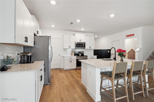 kitchen with white cabinets, sink, light hardwood / wood-style flooring, a kitchen bar, and stainless steel appliances