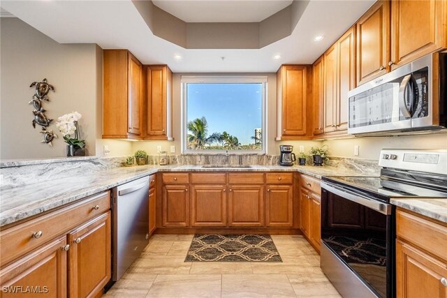 kitchen featuring sink, stainless steel appliances, light stone counters, a tray ceiling, and light tile patterned flooring