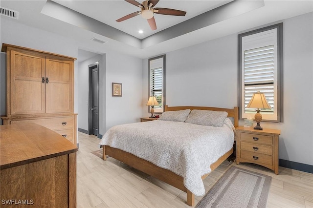 bedroom with a raised ceiling, multiple windows, and ceiling fan