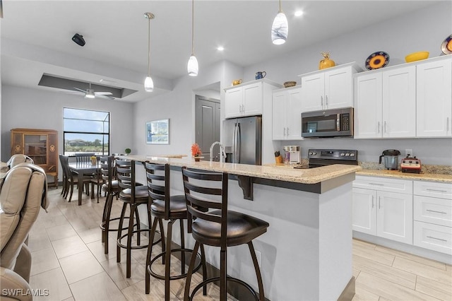 kitchen featuring ceiling fan, an island with sink, decorative light fixtures, white cabinets, and appliances with stainless steel finishes