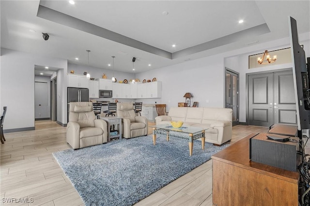 living room with a tray ceiling, a chandelier, and light wood-type flooring