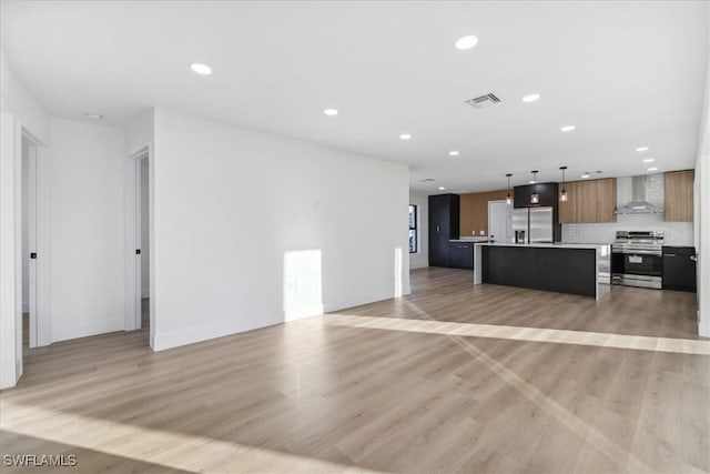 kitchen featuring appliances with stainless steel finishes, a kitchen breakfast bar, hanging light fixtures, a center island, and wall chimney exhaust hood