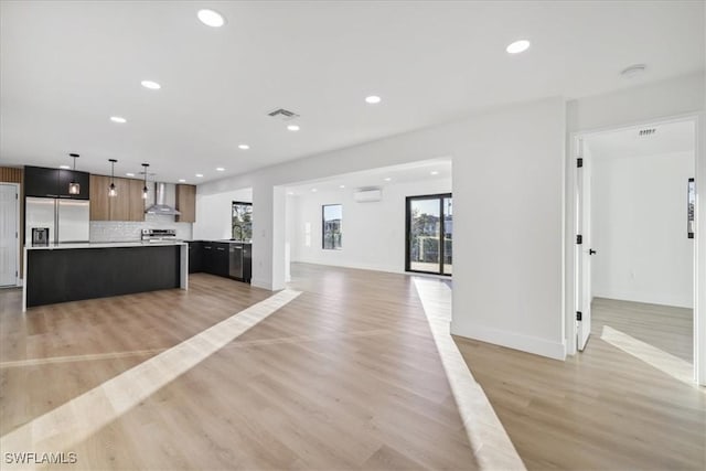 kitchen with a kitchen island, backsplash, hanging light fixtures, stainless steel built in fridge, and wall chimney range hood