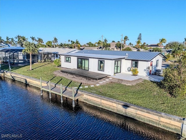 back of house with a water view, a patio area, and a lawn