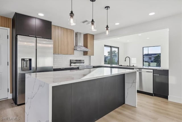 kitchen with pendant lighting, sink, appliances with stainless steel finishes, light stone counters, and wall chimney exhaust hood