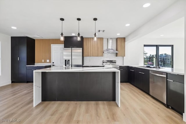 kitchen with a kitchen island, wall chimney range hood, appliances with stainless steel finishes, and hanging light fixtures