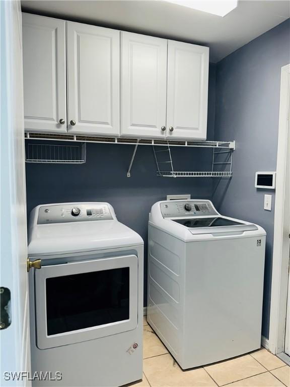 washroom with cabinets, washing machine and dryer, and light tile patterned floors