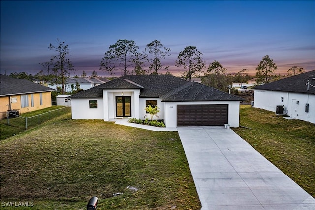 view of front of house featuring a garage, cooling unit, and a lawn