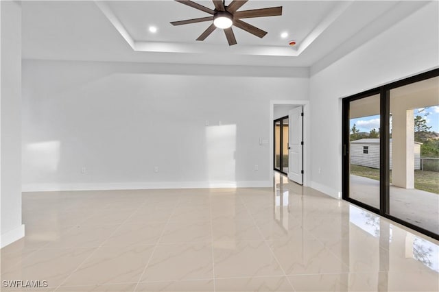 empty room with ceiling fan and a tray ceiling