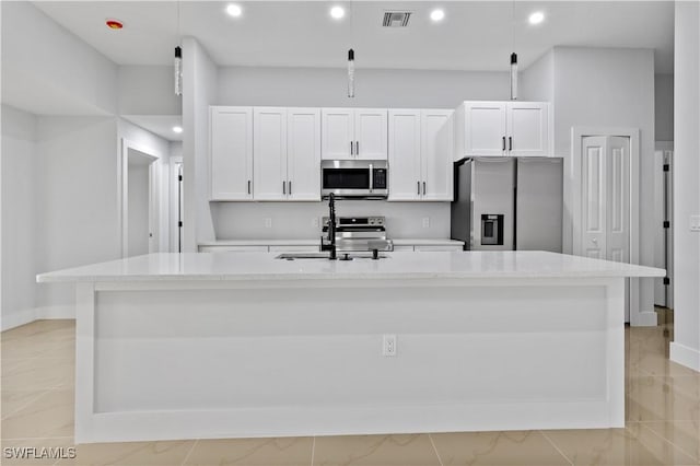 kitchen with light stone countertops, stainless steel appliances, a kitchen island with sink, decorative light fixtures, and white cabinetry