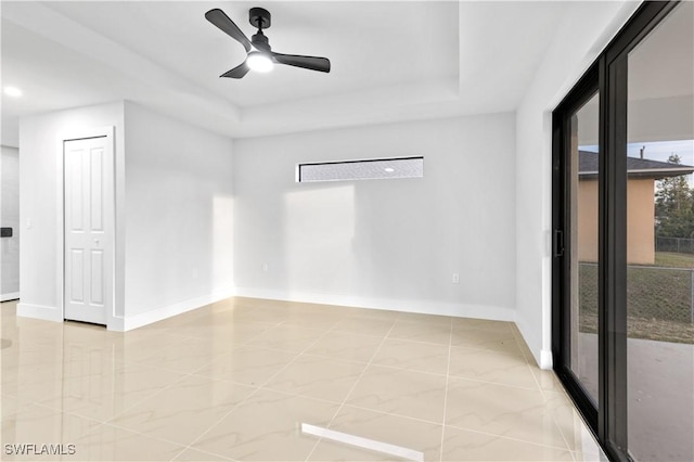 empty room with tile patterned flooring, ceiling fan, and a raised ceiling