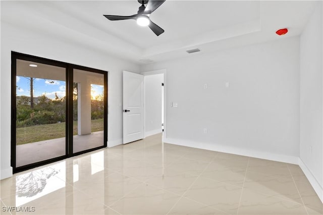 tiled spare room featuring a raised ceiling and ceiling fan