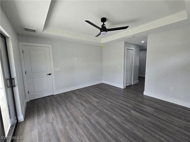 empty room featuring a raised ceiling, ceiling fan, and dark hardwood / wood-style flooring