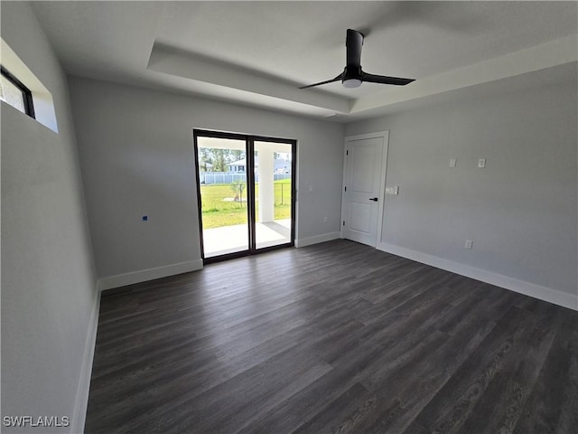 unfurnished room featuring dark hardwood / wood-style floors, ceiling fan, and a tray ceiling