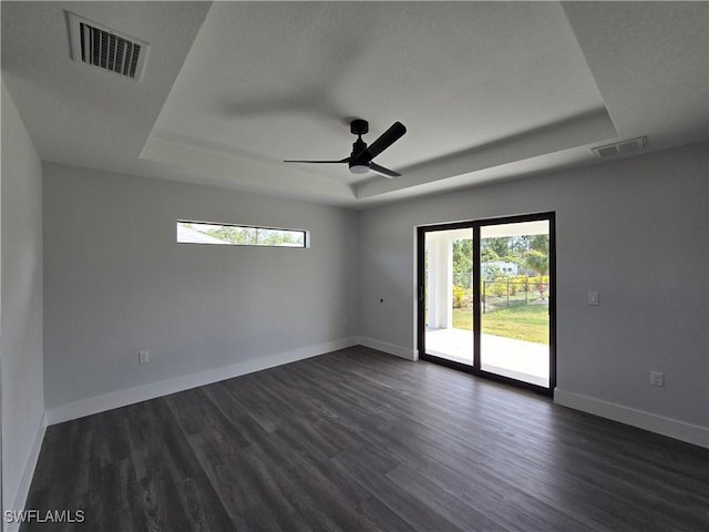 empty room featuring a raised ceiling, ceiling fan, and dark hardwood / wood-style flooring