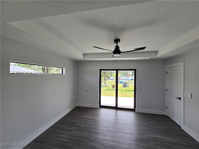 empty room with ceiling fan, dark hardwood / wood-style flooring, and a tray ceiling