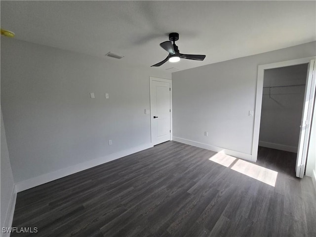 unfurnished bedroom featuring dark wood-type flooring, ceiling fan, a closet, and a walk in closet