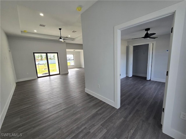 empty room with a tray ceiling, dark wood-type flooring, and ceiling fan