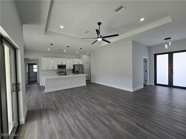 unfurnished living room featuring dark wood-type flooring, a raised ceiling, and ceiling fan