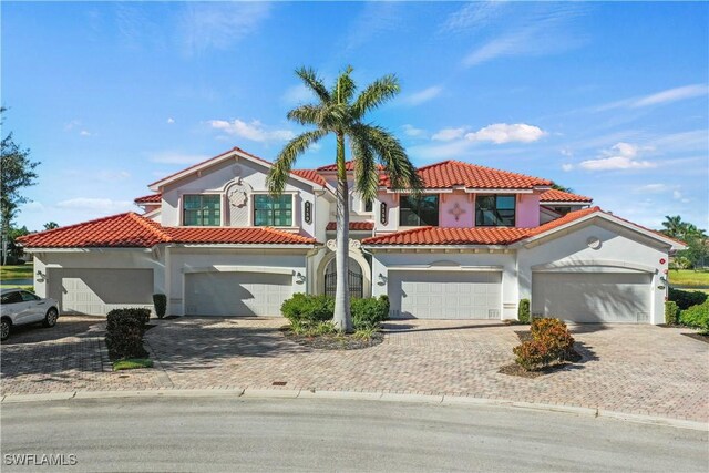 mediterranean / spanish house featuring a tile roof, decorative driveway, and stucco siding